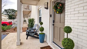 A white brick house with a covered porch, two Adirondack chairs, a red car, and a wreath on the door. - Vibe at The Porter (Ocean Springs)