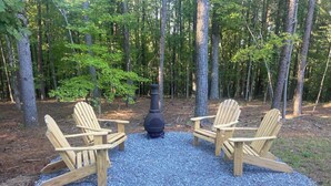 Two wooden Adirondack chairs facing each other with a stone fireplace in the center, surrounded by a forest. - Jasper Short Line
1968 Train Caboose (Jasper)