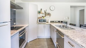 Uma cozinha moderna com armários brancos, bancadas de granito, forno embutido, micro-ondas e pia.