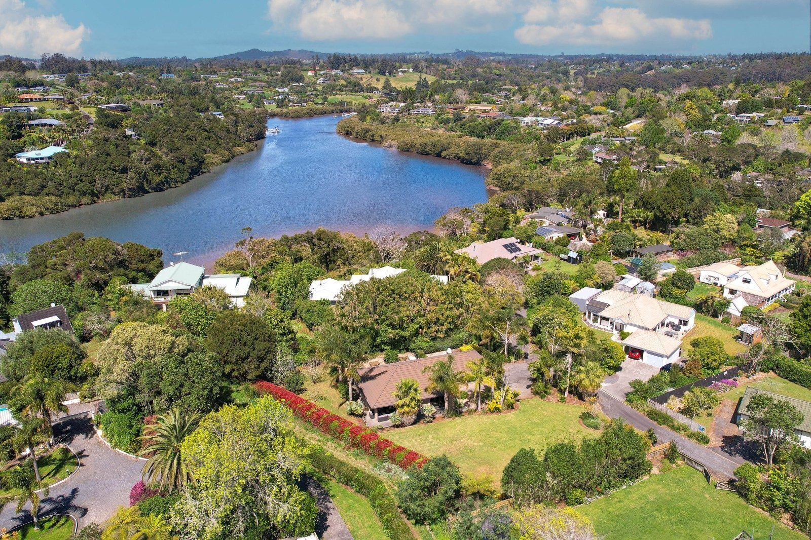 An aerial view of a residential area with houses, a river, and surrounding greenery.