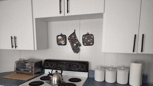 Een keuken met een fornuis, een broodrooster en een waterkoker. Er zijn witte kastjes en een blauw aanrecht.