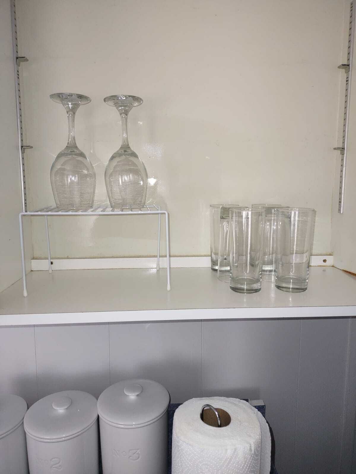 A kitchen area with a white countertop, two wine glasses on a shelf, and several clear glasses on the counter.