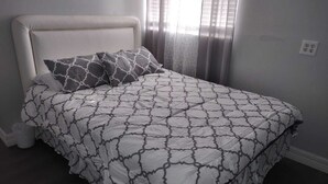 Een bed met een beddegoed met patroon, een kussen met een geometrisch ontwerp en een effen hoofdbord.