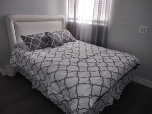 En seng med et mønstret sengetæppe, en pude med et geometrisk design og en ensfarvet sengegavl.