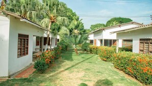 A pathway flanked by two white buildings with red window shutters, surrounded by well-maintained lawns and flowering bushes. - Family cabin in Punta Bolivar, safe condominium near the sea, with parking. (San Antero)