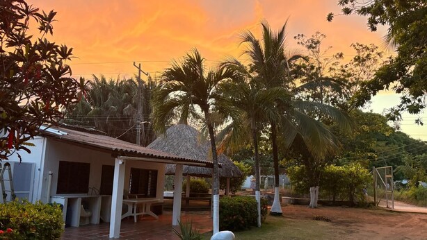 A house with a thatched roof, a covered patio, and a dirt yard with palm trees. - Family cabin in Punta Bolivar, safe condominium near the sea, with parking. (San Antero)