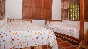 A room with two wooden beds, a large wooden wardrobe, and a window with a view of greenery. - Family cabin in Punta Bolivar, safe condominium near the sea, with parking. (San Antero)