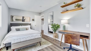 Un dormitorio moderno con cama, mesita de noche, escritorio, silla y estanterías con plantas.