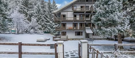 A multi-story building with balconies, surrounded by snow-covered trees.