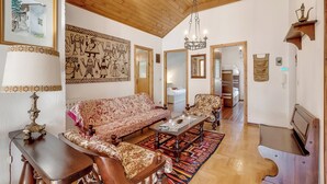 Een ruime woonkamer met hoog houten plafond, een gestreept sofa, een bijzettafeltje en een kroonluchter.