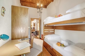 Una habitación con literas, un escritorio con lámpara y una silla. Se observa una puerta de madera y un candelabro.