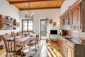 Un coin repas avec une table en bois, des chaises et un lustre. Il y a aussi une cuisine avec des meubles en bois et un téléviseur.