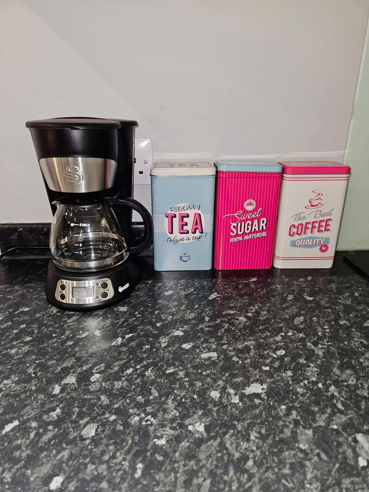 A coffee maker and three containers of tea, sugar, and coffee on a kitchen counter.