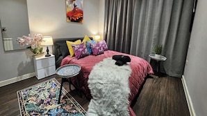 Ein modernes Schlafzimmer mit Bett, Nachttisch, Lampe, Spiegel, Gemälde, Teppich und einem Topf mit Pflanze.