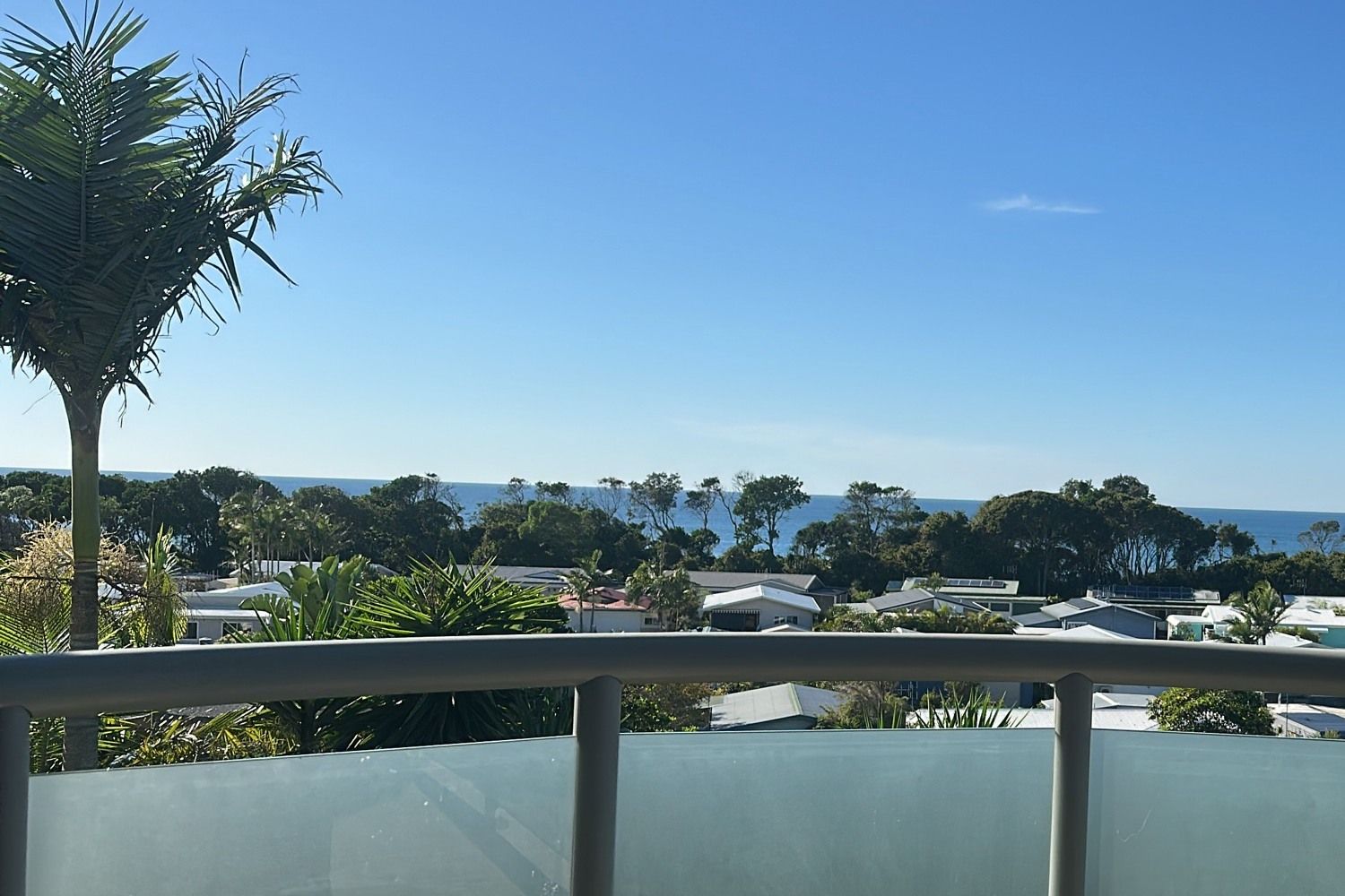 A balcony with a clear view of a residential area, trees, and a body of water.
