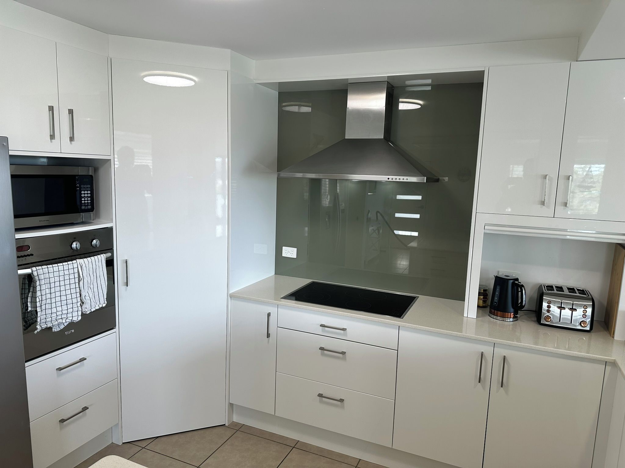 A modern kitchen with white cabinetry, a built-in microwave, oven, and a stainless steel range hood.
