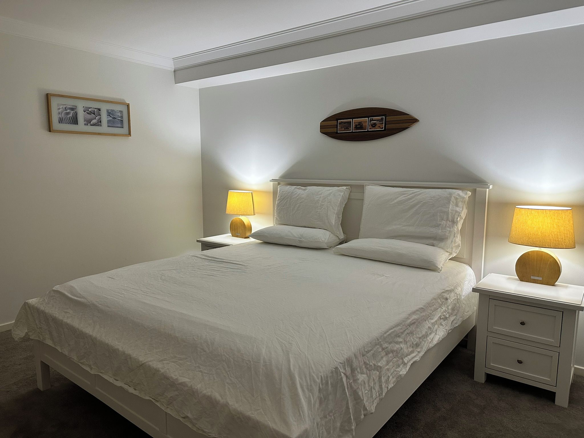 A neatly made bed with white linens, two bedside lamps, and a small wooden nightstand with a drawer.