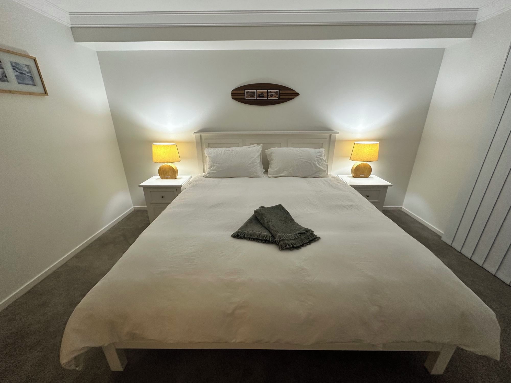Un lit bien fait, avec une couverture pliée, deux lampes de chevet et un tableau encadré accroché au mur.