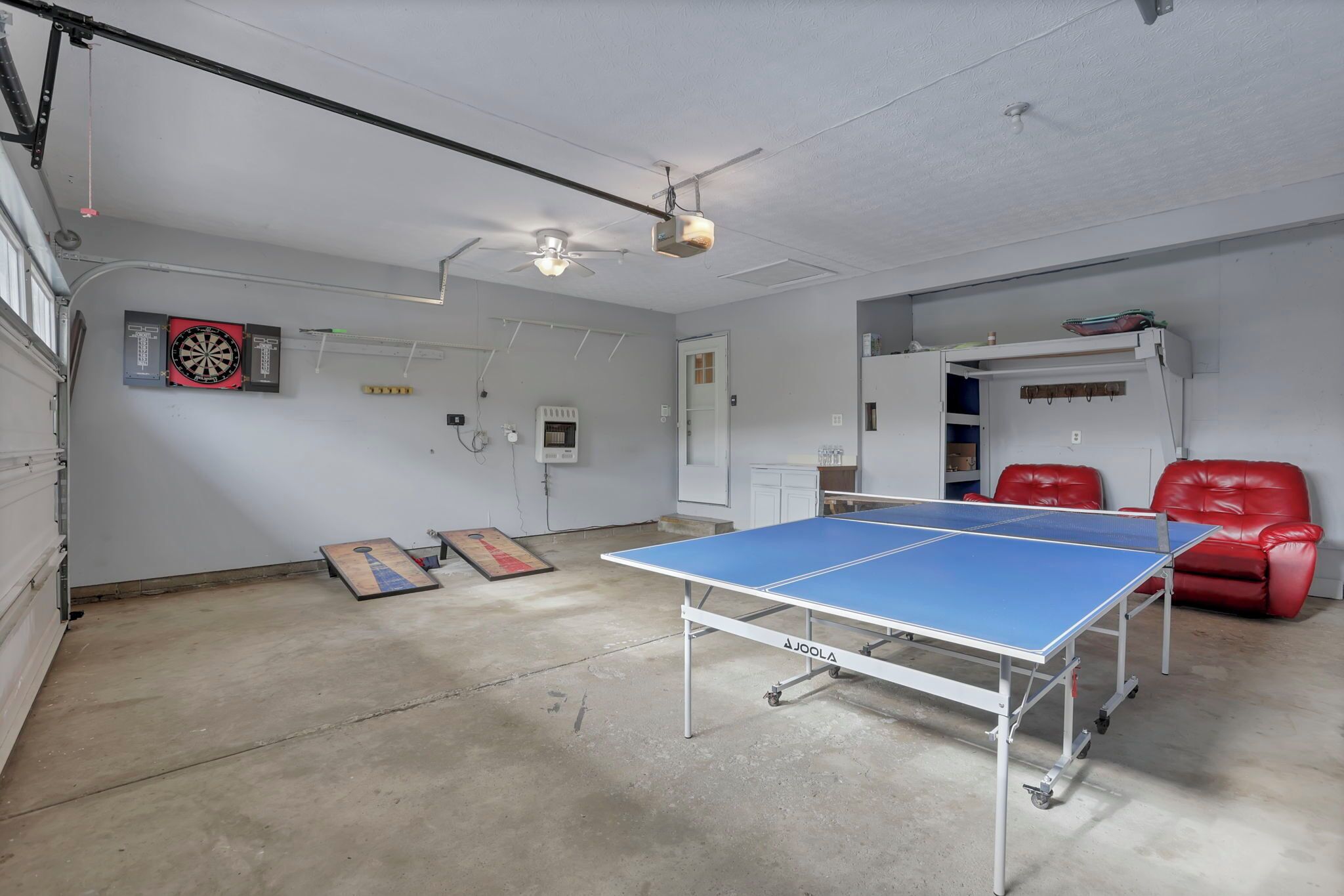 Um quarto com mesa de pingue-pongue, cadeiras de couro vermelho, alvo de dardos e um ventilador de teto.