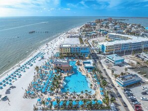 An aerial view of a coastal resort with a large swimming pool, beach, and beachfront buildings. - Soak Up the Sun & Views from Above – Luxe Beach Escape Awaits! - Amazing Penthouse Condo - Roelens (Fort Myers Beach)