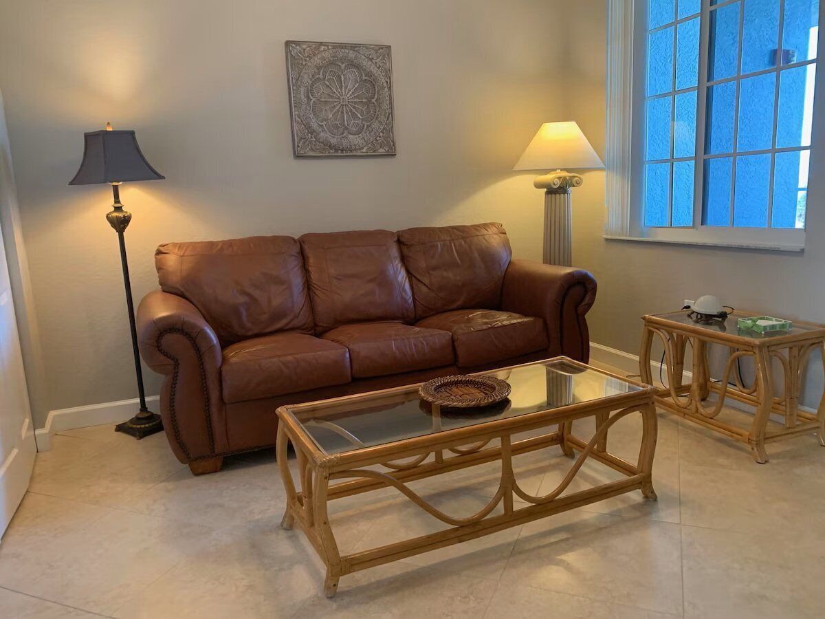 A living room with a brown leather sofa, a glass-top coffee table, a floor lamp, and a side table with a lamp.