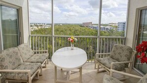 En balkon med et hvidt bord og to mønstrede stole, med udsigt over en by med bygninger og grønne områder.