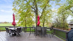 Eine Holzterrasse mit Gartenmöbeln und roten Sonnenschirmen, umgeben von Bäumen und einer Rasenfläche.