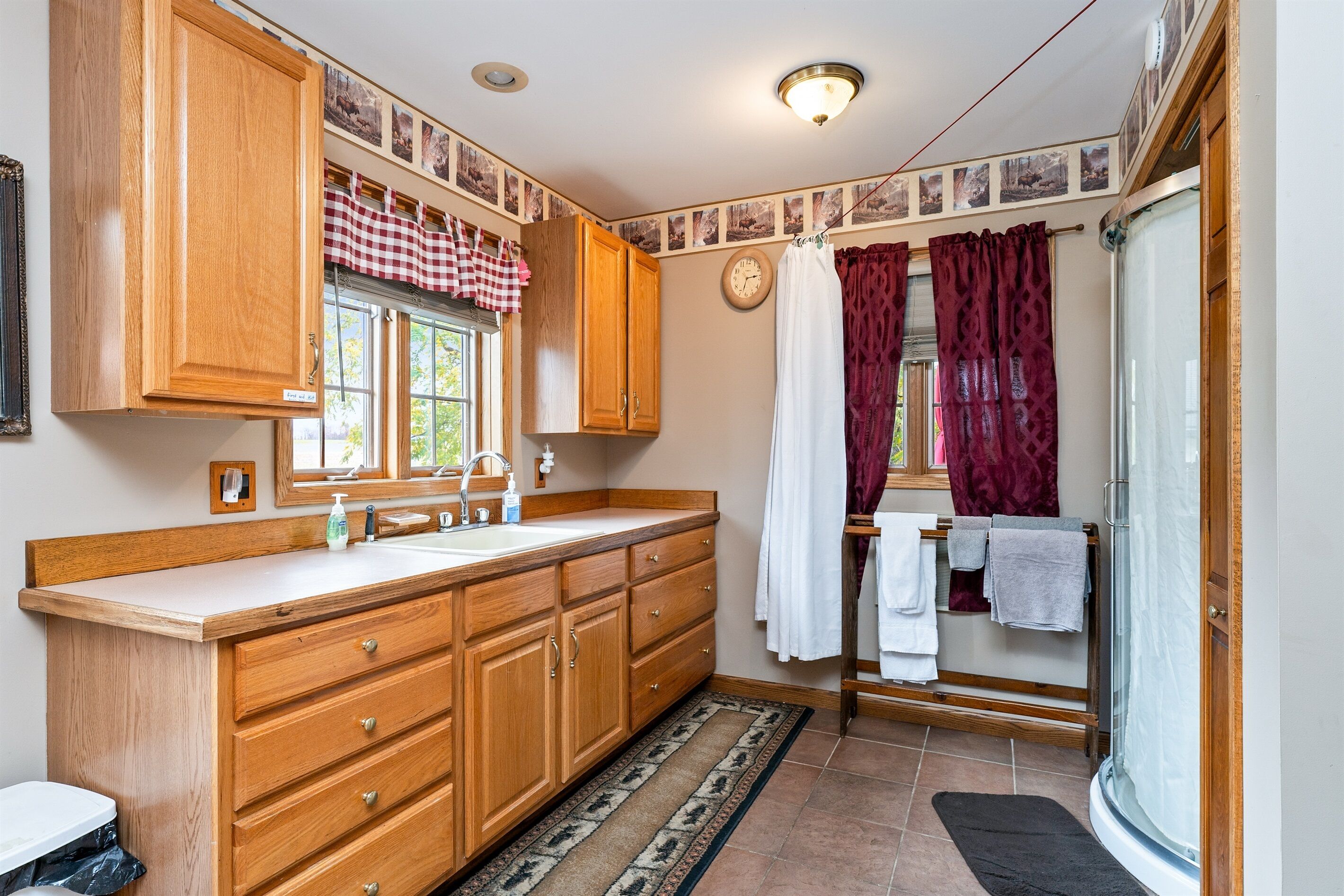 Une salle de bain avec des meubles en bois, un lavabo, un miroir, une douche avec une porte en verre et un porte-serviettes.