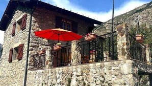 A stone building with a balcony, red umbrellas, and a mountain backdrop. - Country House with stunning views near Porte-Puymorens and Andorra (Carol)