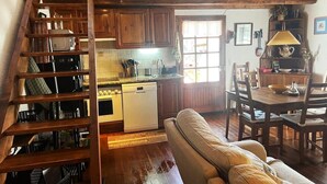 A cozy kitchen with wooden cabinets, a built-in oven, and a dishwasher. There's a dining area with a wooden table and chairs. A staircase with wooden railings leads to another level. - Country House with stunning views near Porte-Puymorens and Andorra (Carol)