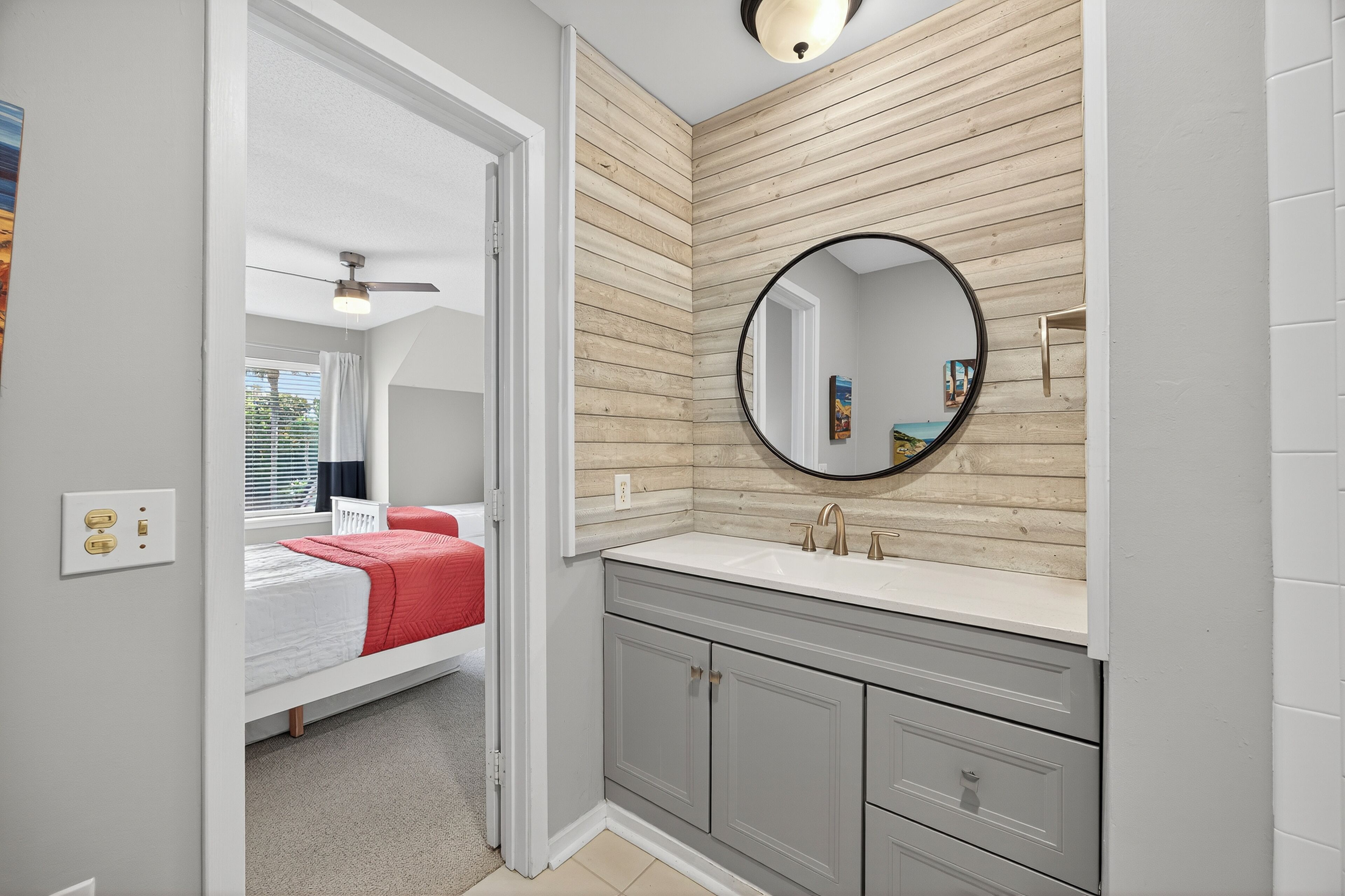 A modern bathroom with a wooden panel wall, a round mirror, and a grey vanity with drawers.