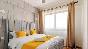 Ein modernes Hotelzimmer mit einem großen Bett, einem grauen Kopfteil und einem Fenster mit Vorhängen.