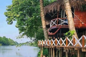 A treehouse with a thatched roof, wooden deck, and a white railing.
