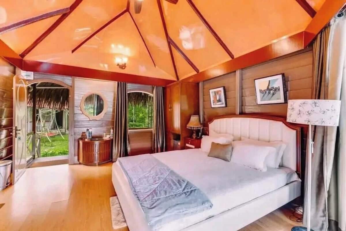 Ein Schlafzimmer mit einem Bett, einem Nachttisch, einer Lampe, einem Spiegel und einem Fenster.
