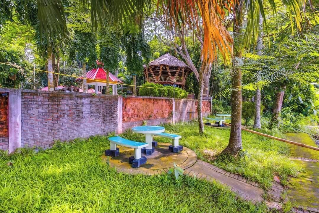 Um espaço de jardim com muro de tijolos, uma construção com telhado de colmo e duas bancas azuis.