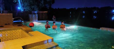 En swimmingpool med klart vand, et boblebad og et terrassedæk i træ.