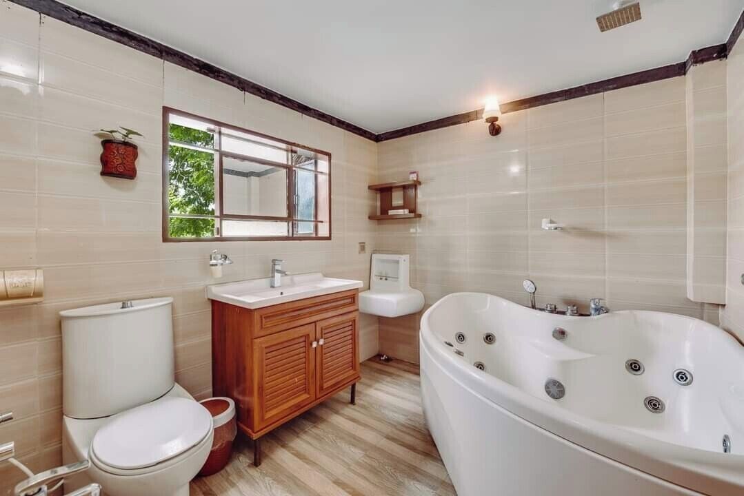 A bathroom with a toilet, sink, vanity, bathtub, and a window.