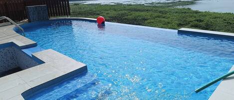 A swimming pool with steps leading into it, surrounded by greenery and a view of a body of water.