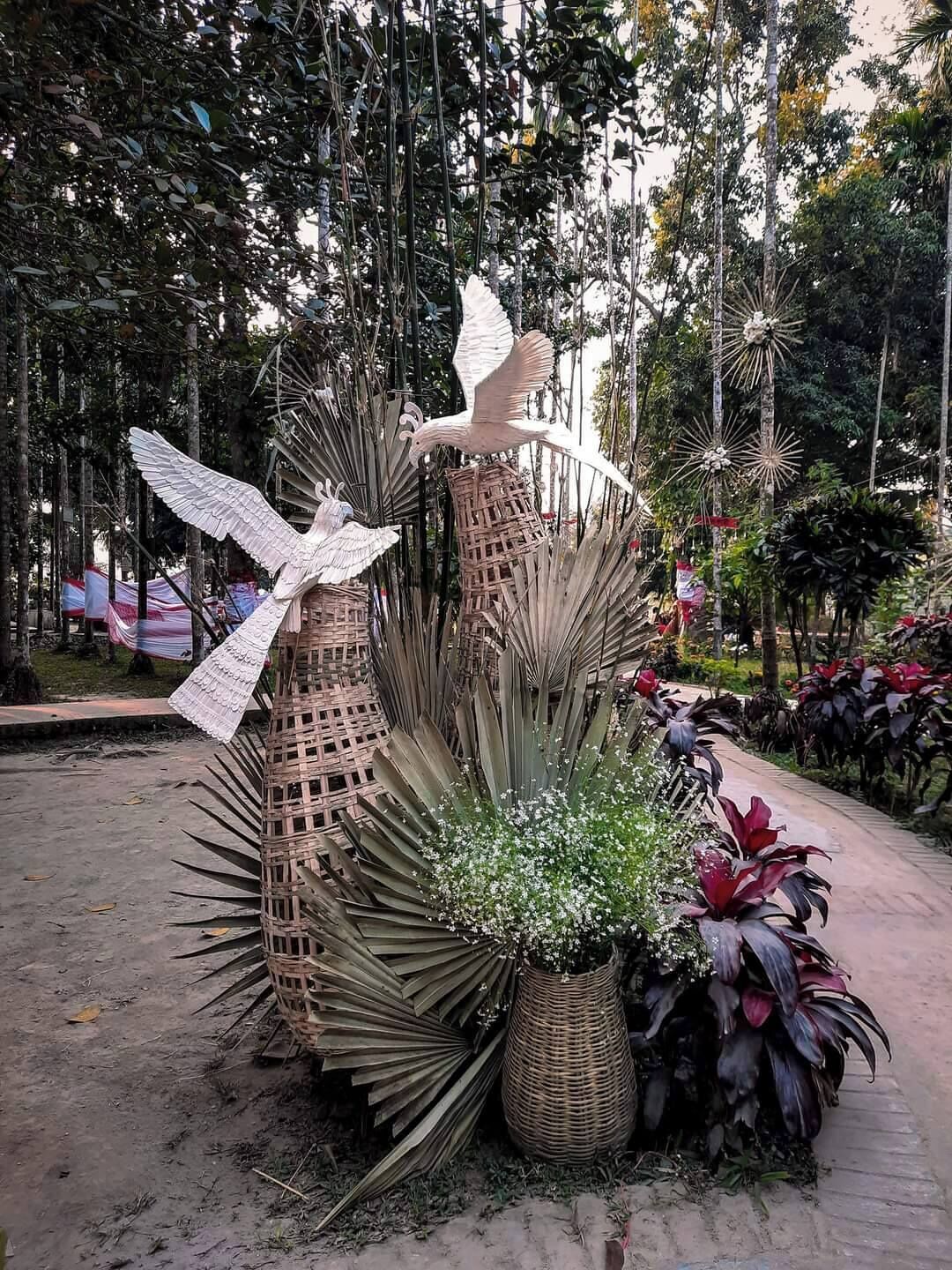 Un jardín con esculturas decorativas de aves, una cesta tejida y diversas plantas.