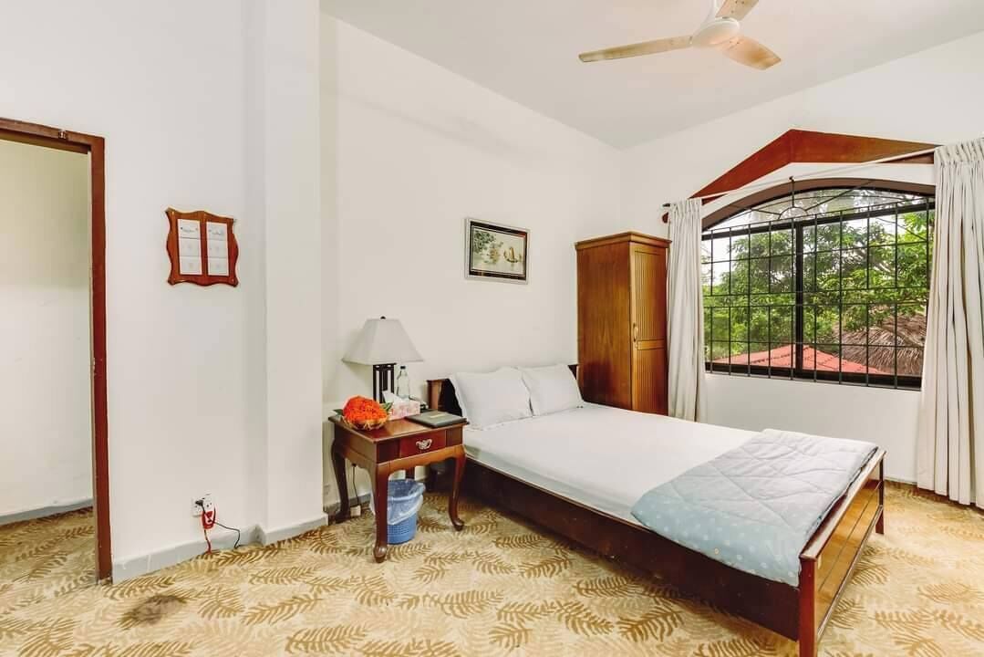 A bedroom with a bed, a nightstand, a wardrobe, a window with curtains, and a ceiling fan.