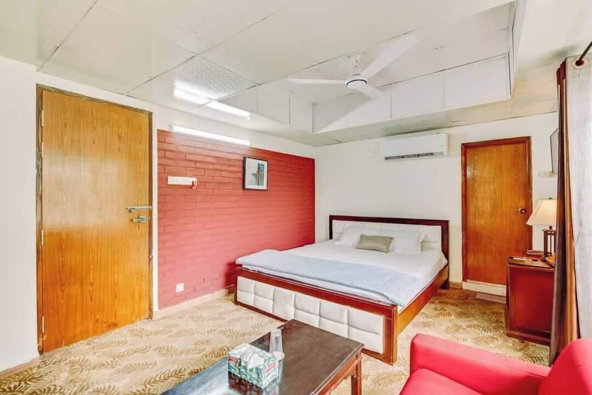 Ein Hotelzimmer mit einem Bett, einer Holztür, einer roten Backsteinwand, einem Deckenventilator und einem kleinen Tisch.