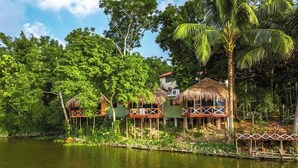 Accommodatie aan de rivier met rieten hutten, omgeven door weelderige begroeiing en een rustige rivier.