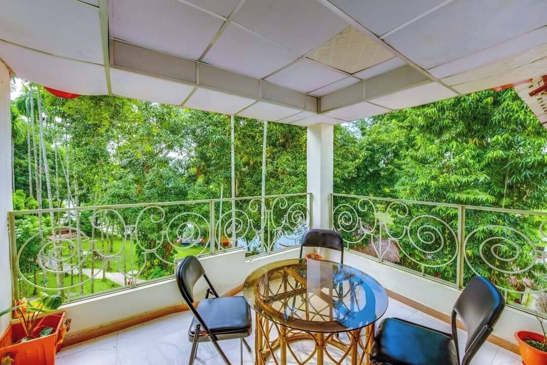 A balcony with a round table and chairs, surrounded by a metal railing, overlooking a lush green garden.