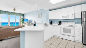 Una cocina moderna con armarios blancos, una isla central y vistas al océano.