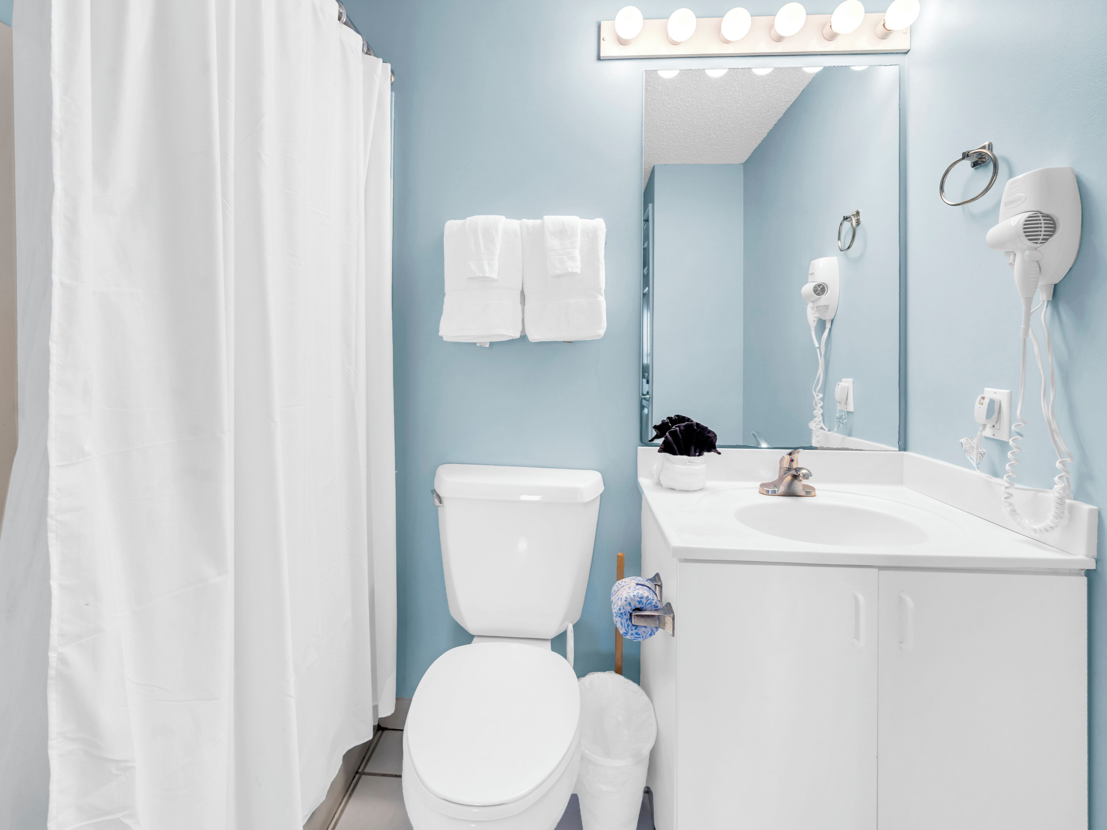 A bathroom with a white toilet, a sink with a mirror, and a hairdryer.