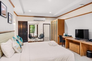 Quarto de hotel com cama, escrivaninha com televisão, uma cadeira e guarda-roupa.