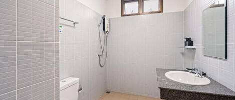 A small, clean bathroom with white tiles, a toilet, a sink, and a shower.