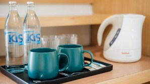 Zwei klare Glasflaschen, zwei türkisfarbene Tassen und ein weißes Wasserkocher auf einer Ablagefläche.