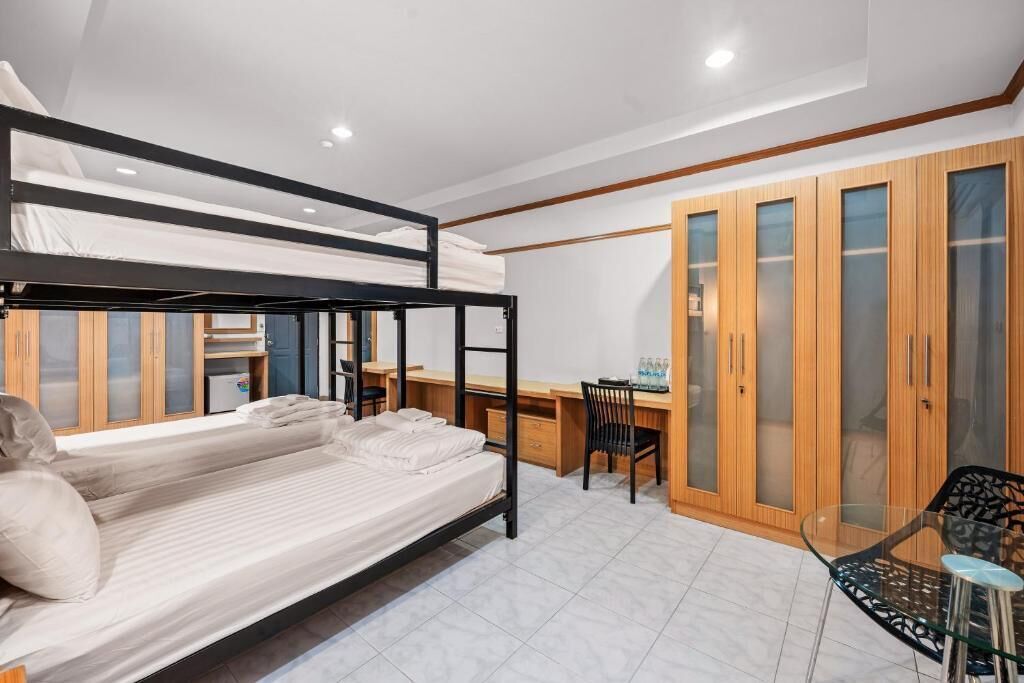 A bunk bed room with a desk and chair, wooden wardrobe, and a glass table.