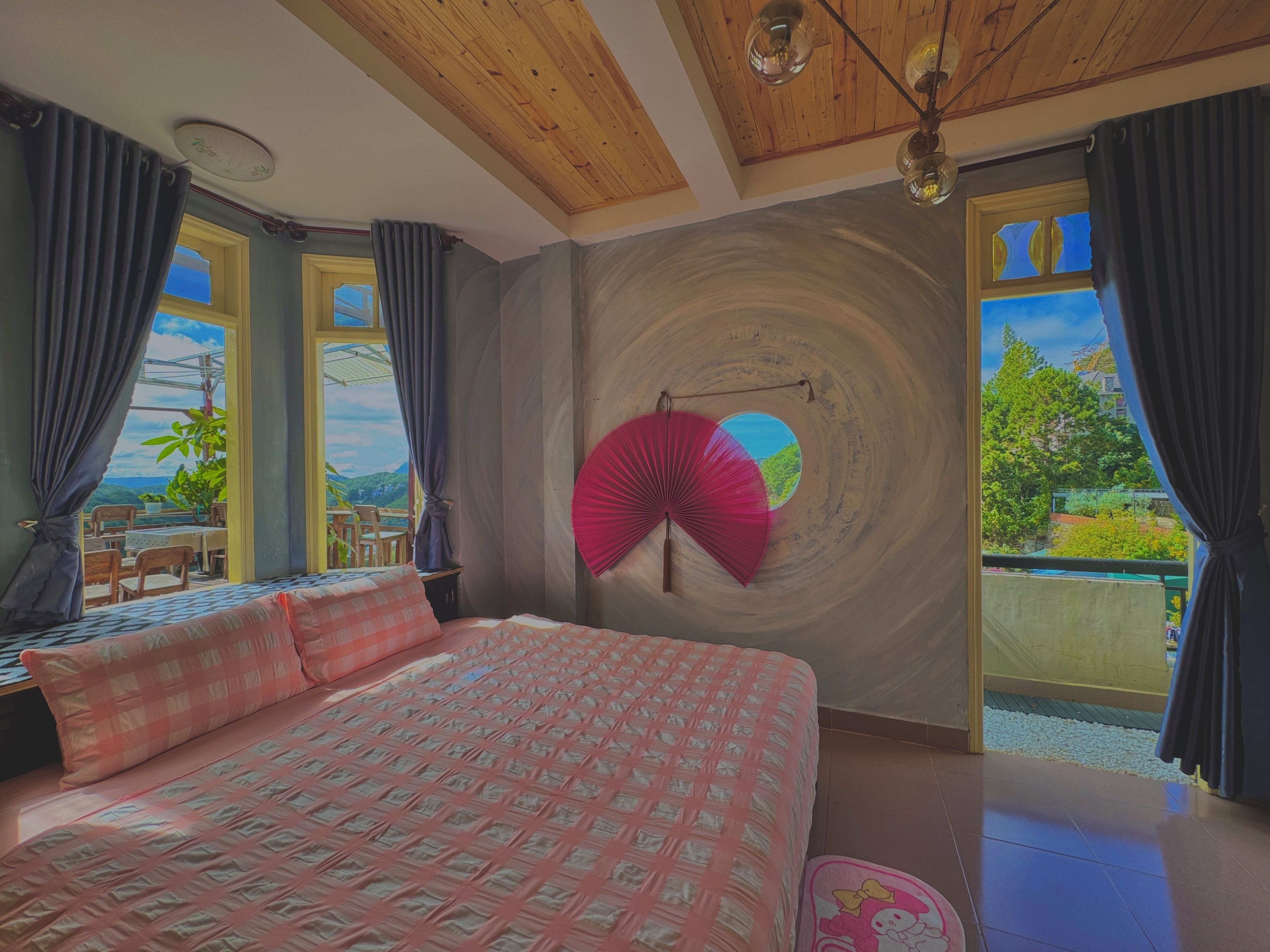 A bedroom with a large bed, a view of the outdoors through a window, and a ceiling fan.